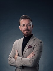 Obraz premium Portrait of a stylish elegant senior businessman with a beard and casual business clothes in photo studio isolated on dark background gesturing with hands