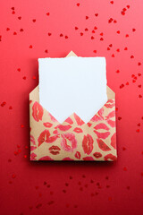 Envelope with lipstick marks and blank paper note inside on red background, top view. Romantic, Love letter concept. Happy Valentines Day greeting card mockup.