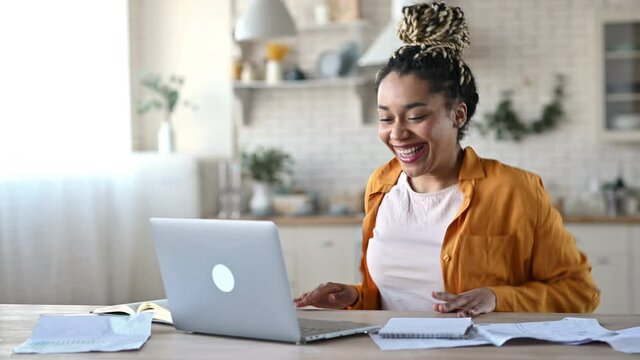 Overjoyed excited african american girl with dreadlocks, freelancer, manager working remotely at home using laptop, looks at screen with surprise, smiling face, gesturing with hands, got a dream job