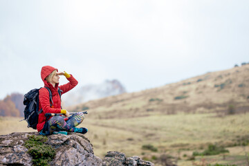 Hiker girl taking a rest on a rock in the mountains. Enjoying the view. Travel and healthy...