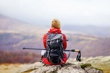 Hiker girl taking a rest on a rock in the mountains. Windy day. Travel and healthy lifestyle...