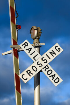 Railroad crossing sign against blue moody sky with barrier upright