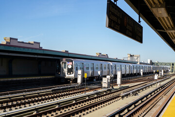 F subway train approaching elevated station in Brooklyn, New York. Train tracks on the outdoor platform - Powered by Adobe