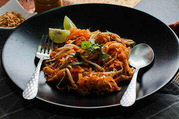 Thai Food Pad Thai (Thai national dish) Pad Thai on black plate with lime and seasonings.