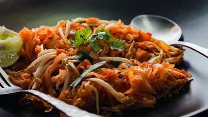 Thai Food Pad Thai (Thai national dish) Pad Thai on black plate with lime and seasonings.