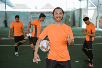 Male futsal player smiling with thumbs up carrying the ball