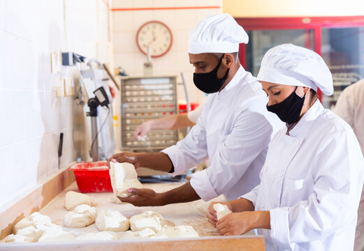 Young Latina working with husband in small family bakery, shaping dough on floured surface before baking