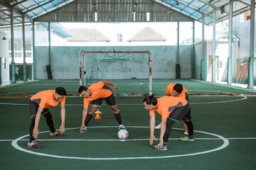 four futsal players stretching their legs in the middle court