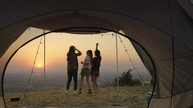 group of young Asian friends standing and taking pictures and relaxing in front of a tent during a summer camping vacation in the evening when the sunset. concept of freedom, leisure, travel, adventur