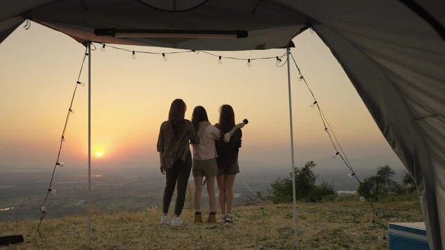 group of young Asian friends standing and taking pictures and relaxing in front of a tent during a summer camping vacation in the evening when the sunset. concept of freedom, leisure, travel, adventur