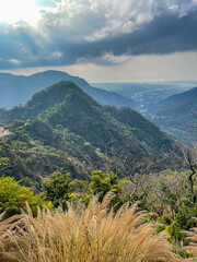 View of cloud formation, mountain ranges  and river flowing in the background and dry grass in the foreground
