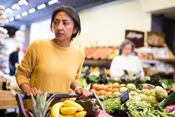 Positive woman choosing food products on shelves in grocery shop