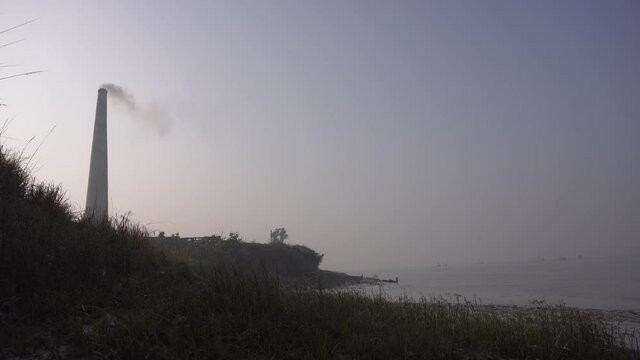 Smoke is coming out of the furnace which is mixed with the air. Which is situated in the riverside.