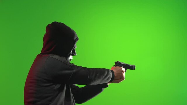 Masked Man in black hooded sweater holding up gun and pointing at you. Shot in Green Screen