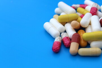 A pile of medicines of different sizes and colors lie on a blue background.