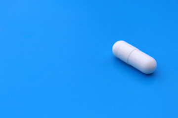 The drug in a white capsule lies alone on an isolated blue background.