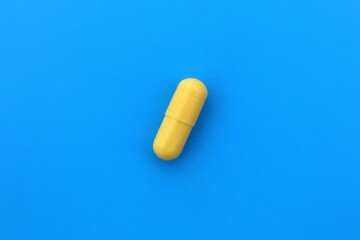 The drug in a yellow capsule lies alone on an isolated blue background.