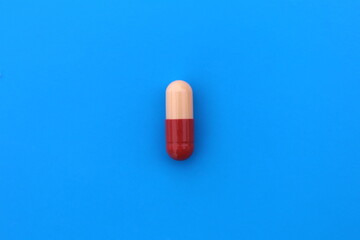 The drug in a two-color capsule lies alone on an isolated blue background.