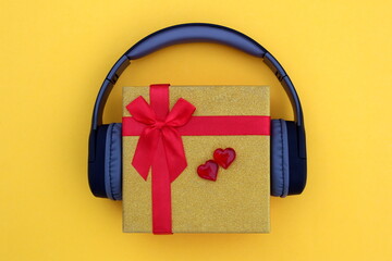 Gift box with valentine and headphones on a yellow background.
