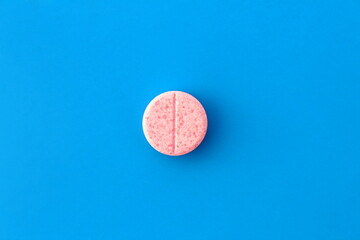 One pink pill lies on a blue background.