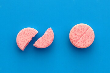 One pink whole tablet lies next to a broken one on a blue background.