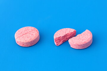 One pink whole tablet lies next to a broken one on a blue background.