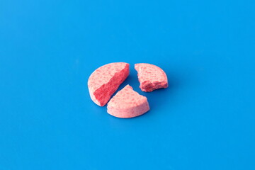 A broken pink pill lies on a blue background.