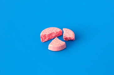 A broken pink pill lies on a blue background.