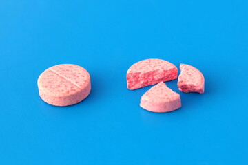 One pink whole tablet lies next to a broken one on a blue background.