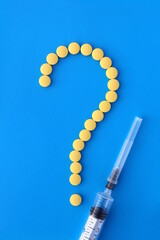 A question symbol is lined with yellow pills on a blue background and a syringe lies nearby.