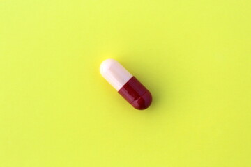 The drug in a capsule beige with burgundy color lies alone on an isolated yellow background.