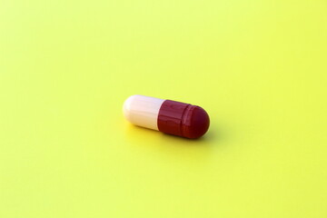 The drug in a capsule beige with burgundy color lies alone on an isolated yellow background.
