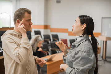 The girl and the guy talk in sign language. Two deaf students chatting in a university class.