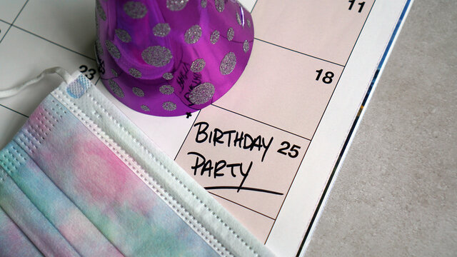 Birthday party written on a calendar, along with party hat and disposable mask indicating the new normal
