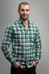 Portrait of a smiling man in a green plaid shirt on a gray background.