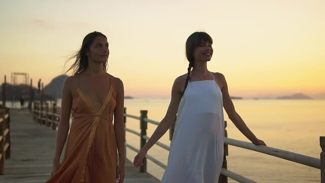 Two young woman models are walking in the evening pier during sun set time, evening dress