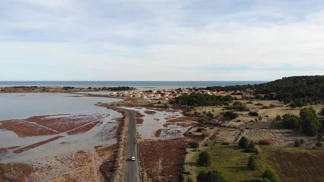 Aerial: car going through a flat road among a marsh and heading for a coastal town by the mediterranean sea in southern France