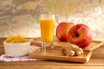 Glass of yellow flavor mixed fruit and herb juice serves in tray with mango, apple, and ginger on...
