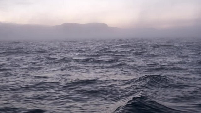 View from the ship to the coast and the surface of the Barents Sea at sunset. Beautiful waves and mountains in winter