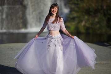 Naklejka premium a beautiful young girl in a magnificent dress dances against the backdrop of a waterfall, a story about a forest elf