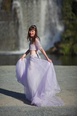 Fototapeta premium a beautiful young girl in a magnificent dress dances against the backdrop of a waterfall, a story about a forest elf
