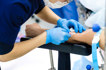 The doctor inserts a dropper needle into a vein in the patient's arm. Selective focus. Doctor in sterile gloves and a protective mask. Intravenous administration of drugs through a catheter. 
