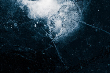 Transparent surface of the ice with cracks and frozen air bubbles on black background.
