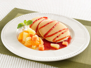 stack of pancakes with strawberry sauce and mixed fruit salad in white plate on green place mat on white back ground.