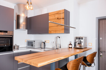 Modern kitchen interior with lights on. Brown wooden table and bar stools, coffee machine. Contemporary interior with loft elements