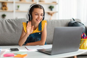 Girl in headphones using laptop, waving to webcam