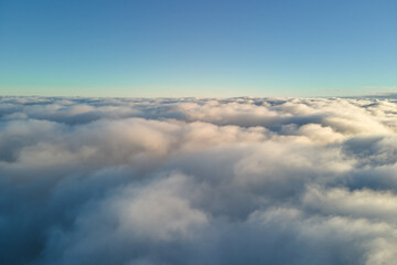 Fototapeta premium Aerial view from airplane window at high altitude of dense puffy cumulus clouds flying in evening
