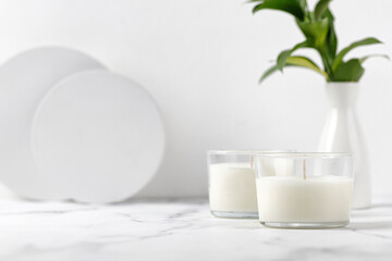 Two jars candles with coconut or soy wax on table with vase of green leaves. White interior pfotography