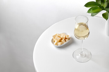 White wine in rich glass on a white round table with cheese vase of greens. Minimalism. Elegant