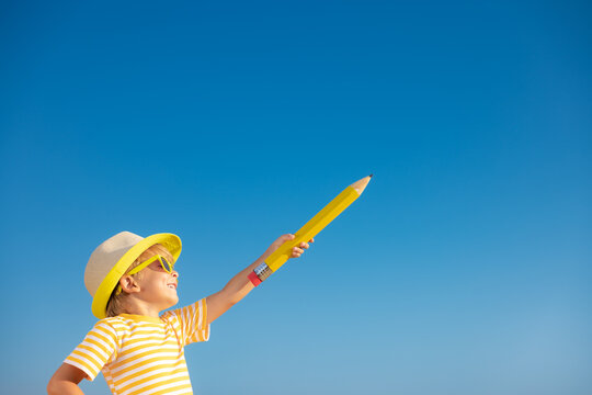 Happy child holding giant pencil outdoor against blue sky